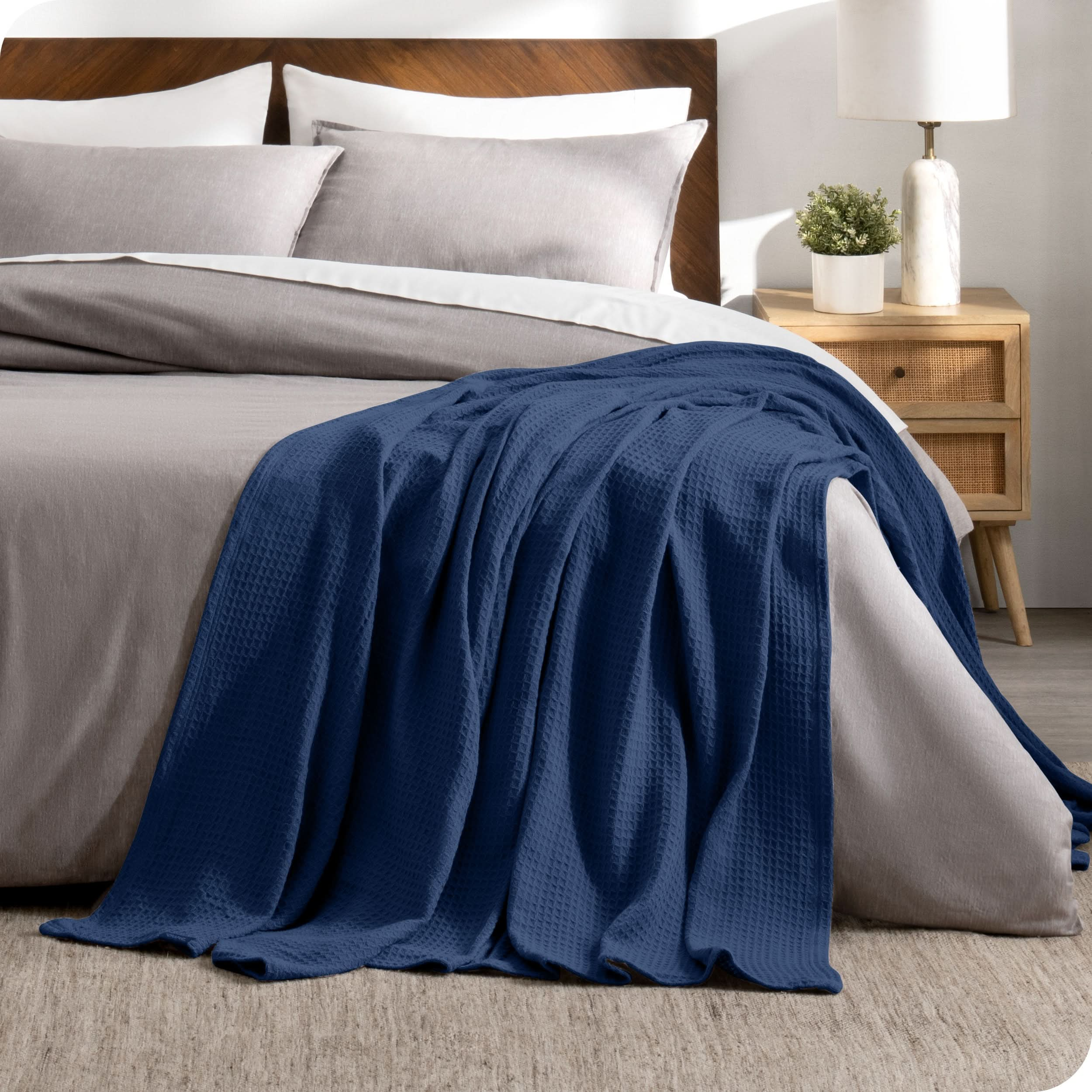 A cotton waffle blanket is on the corner of a bed. It is hanging down the side and end of the bed.