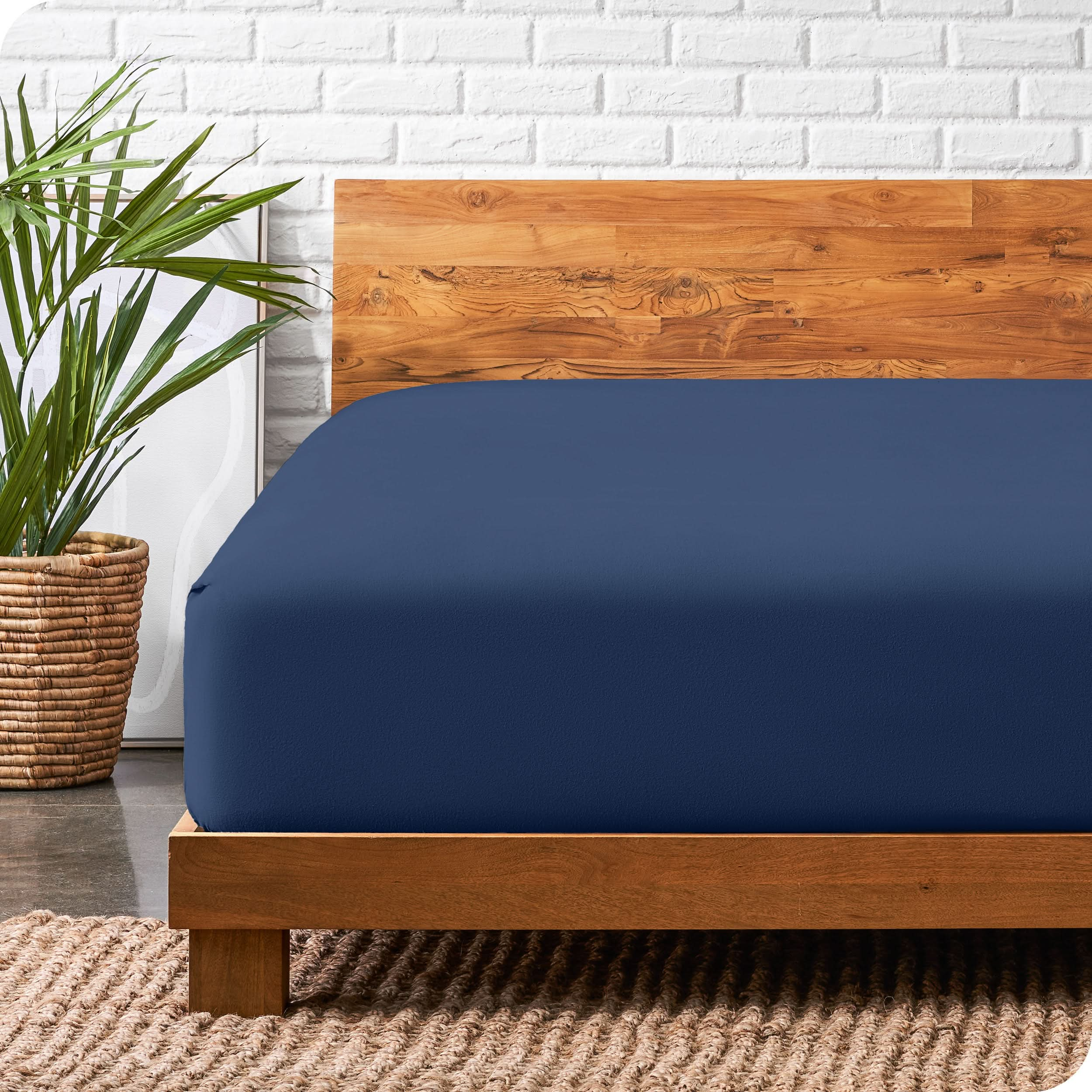 A modern bed with a wooden bed frame with a flannel fitted sheet on.