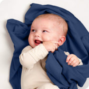 A baby lying on a receiving blanket. She has her thumb in her mouth.