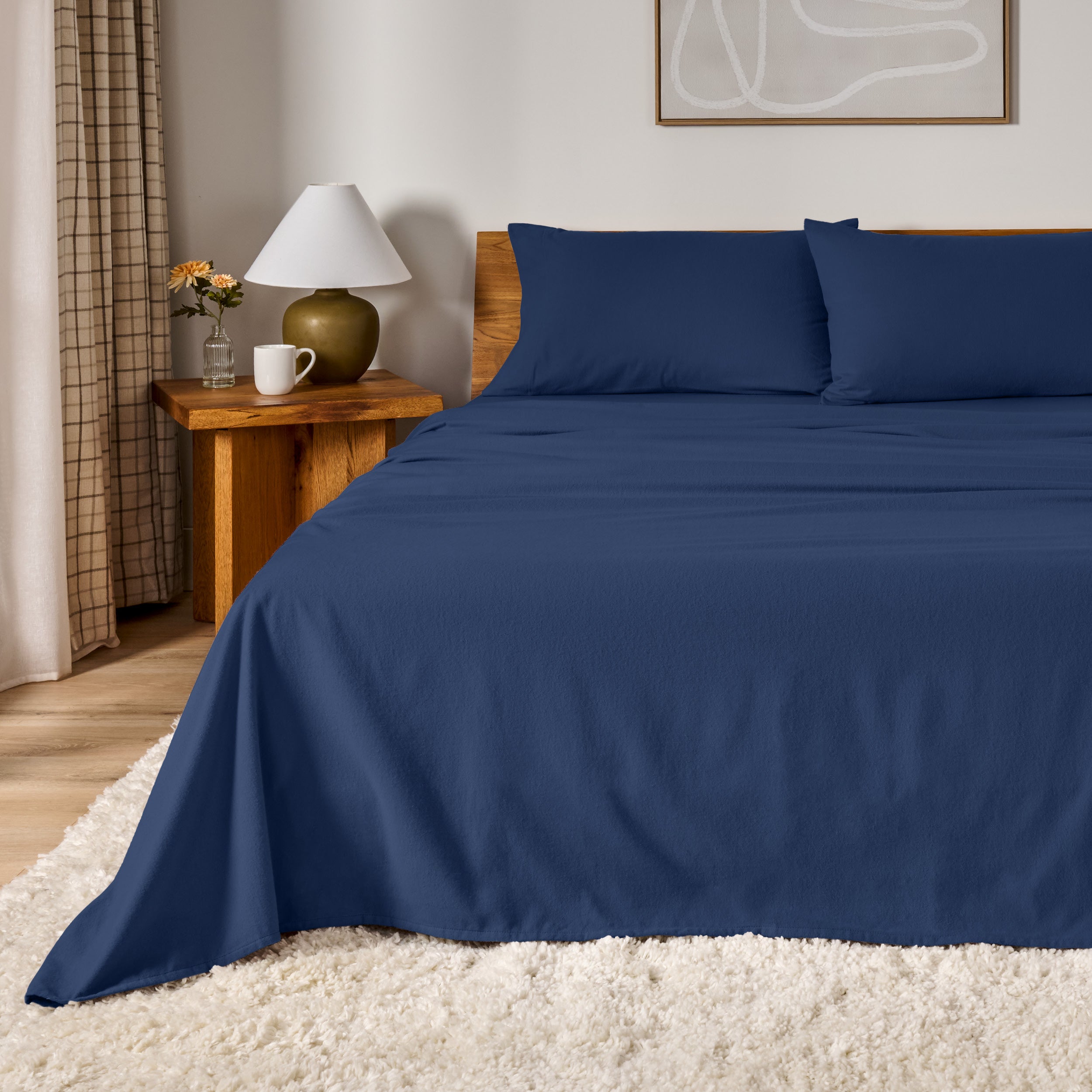 A bed dressed in flannel sheet set in a bedroom with a wooden headboard, bedside table and lamp