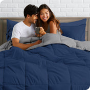 A couple sitting in a bed made with a reversible comforter and sheet set