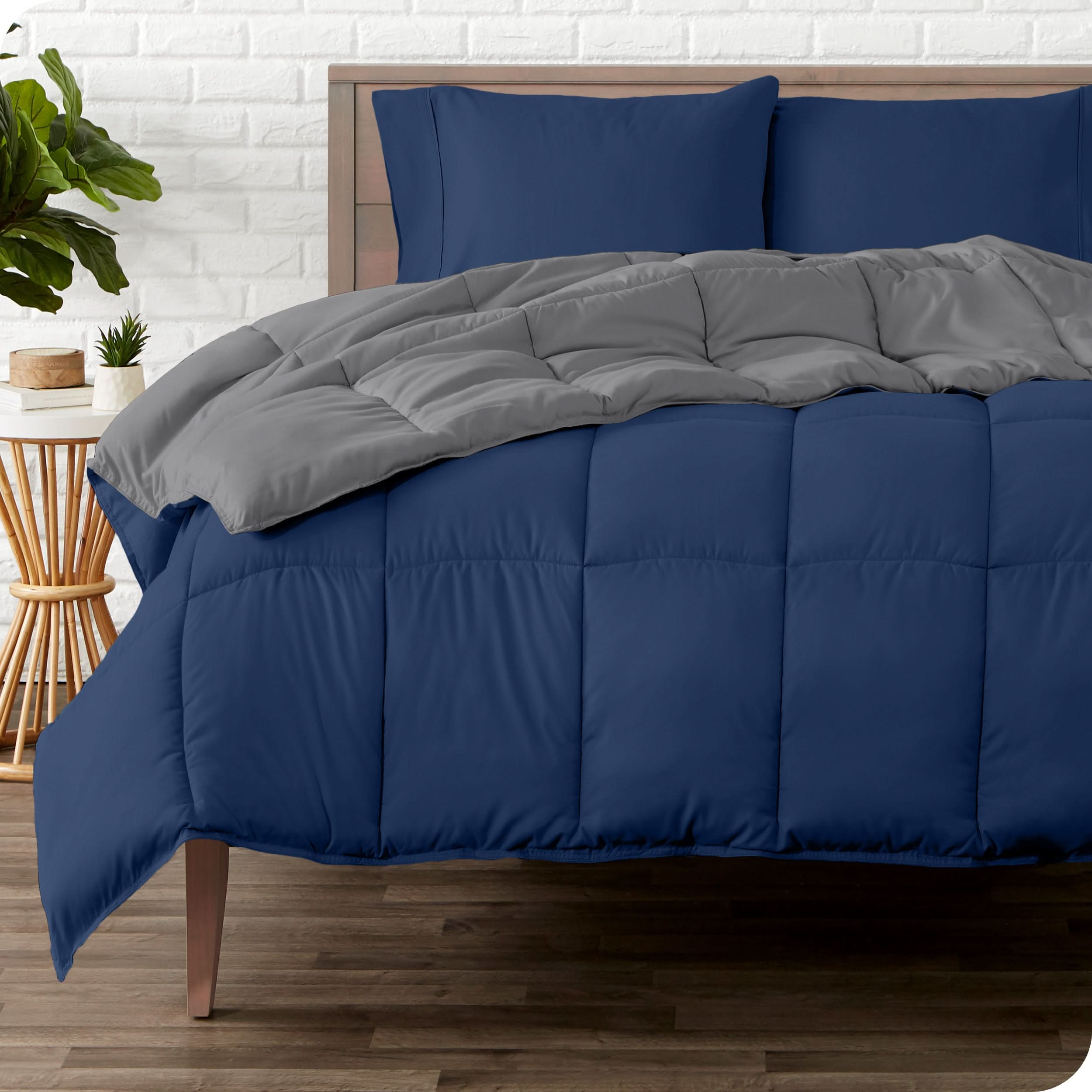 A wooden bed frame with a reversible comforter and sheet set on the mattress