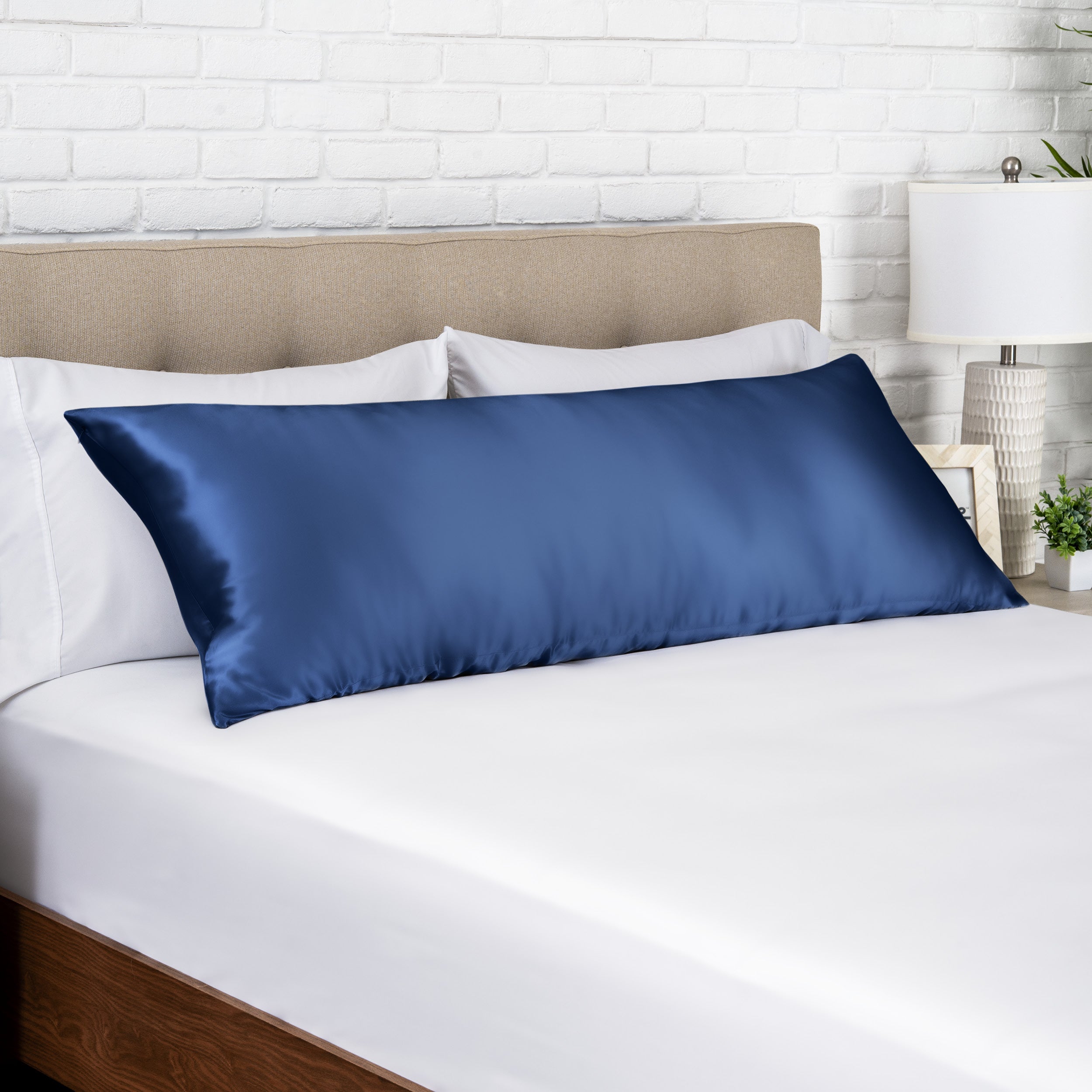 Dark blue silk pillow on a bed with white bedding and a beige headboard.