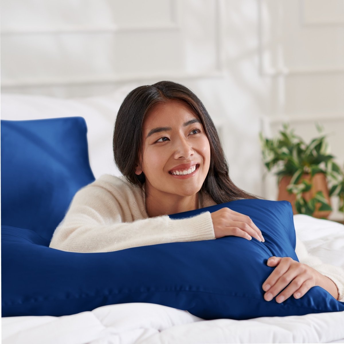 Woman lying on a bed with a body pillow, smiling.