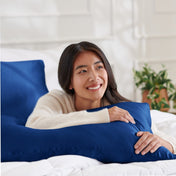 Woman lying on a bed with a body pillow, smiling.