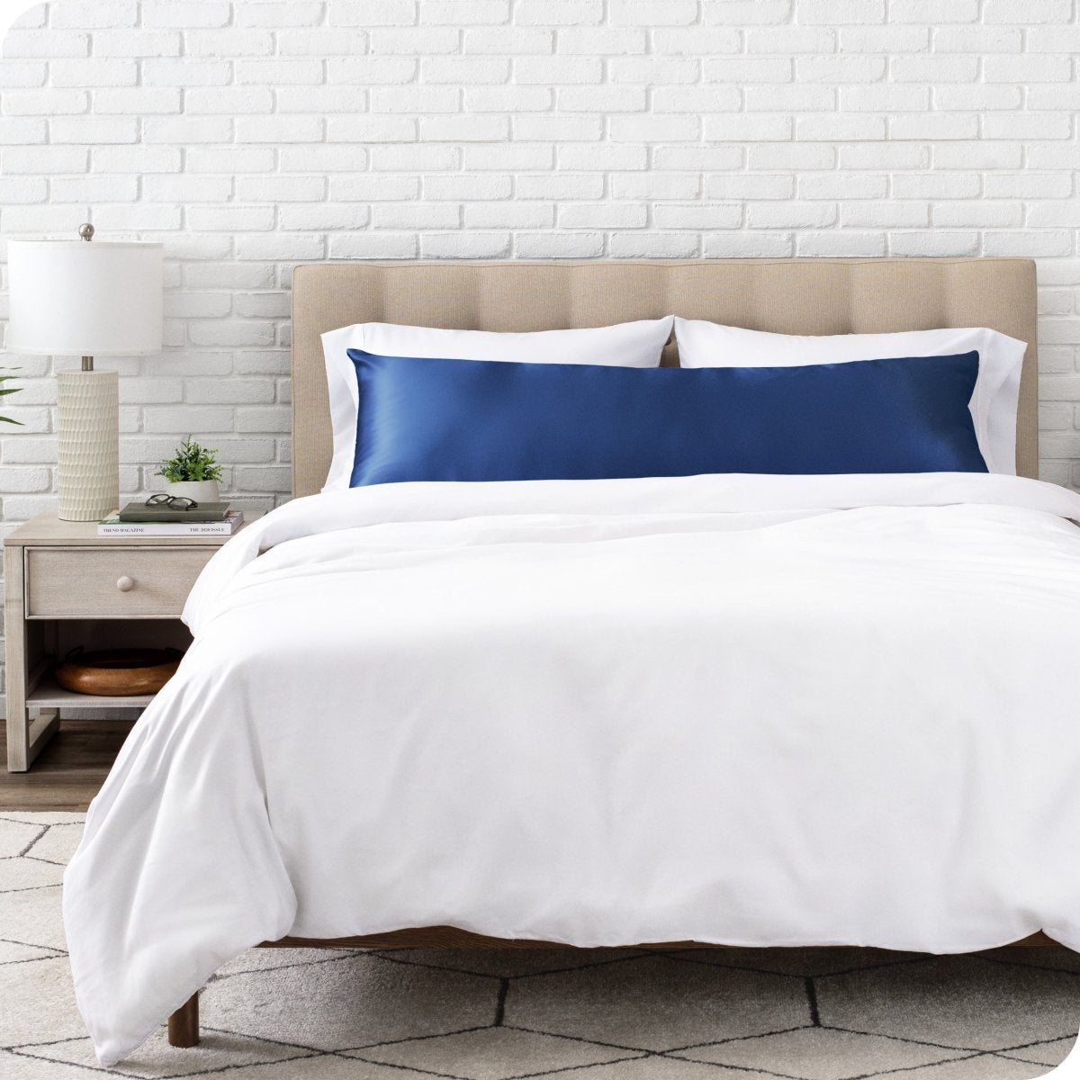 Bed with white bedding and satin pillowcase against a white brick wall.