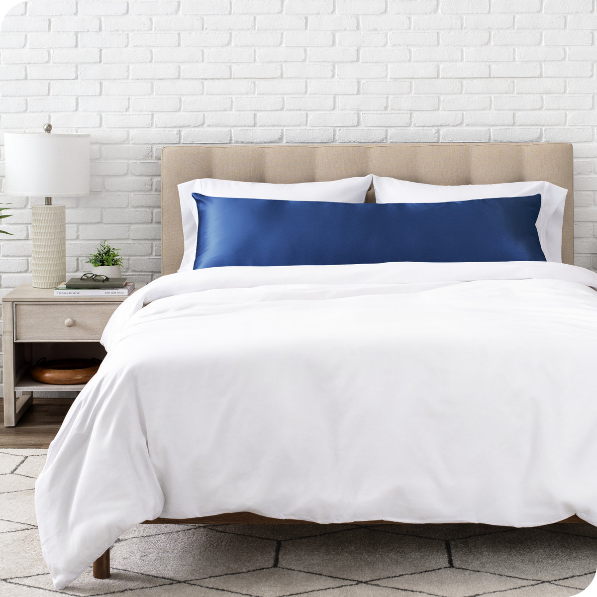 White bedding set with body pillow covered with a silk pillowcase on a bed in a bedroom setting.