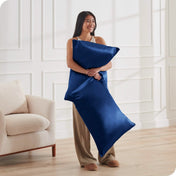 A woman standing while holding pillows with silk pillowcases on them