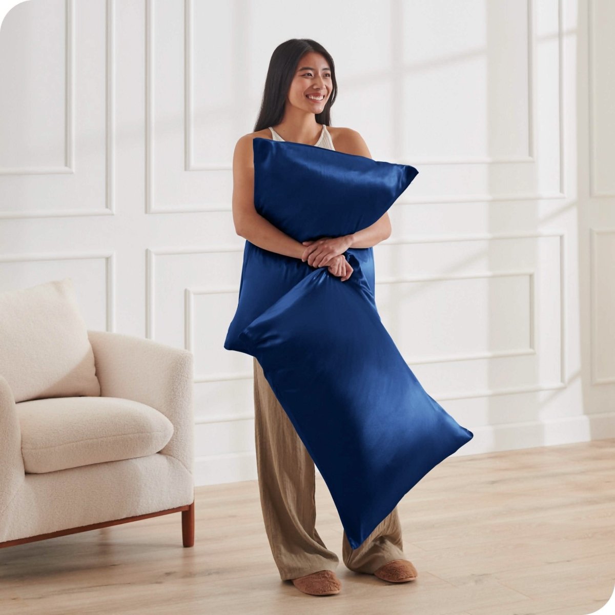 A woman standing while holding pillows with silk pillowcases on them