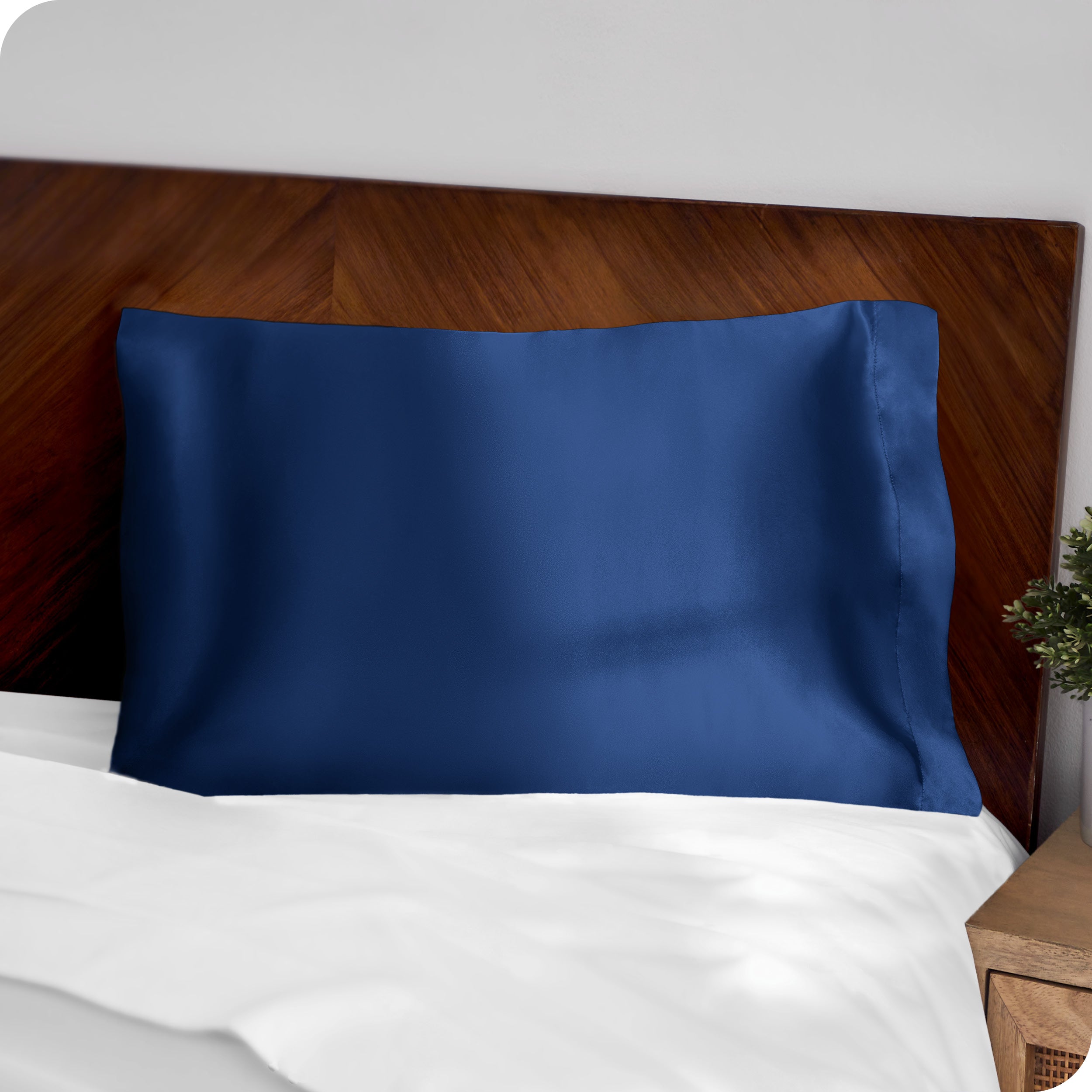 A dark blue silk pillowcase on a pillow resting on a headboard