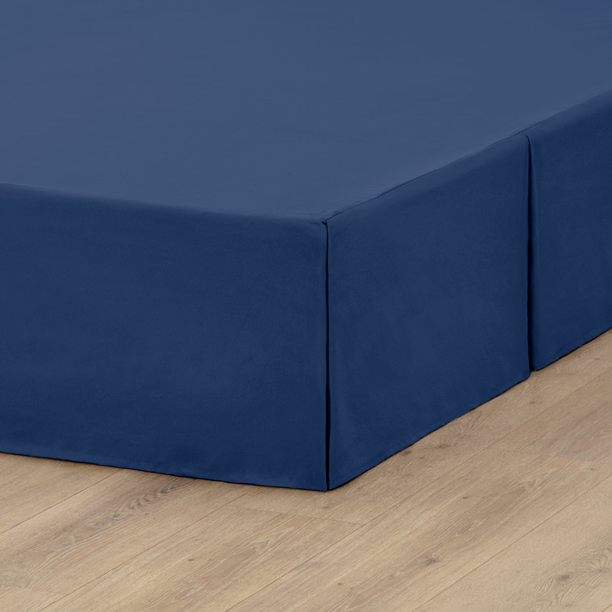 The corner of a box spring with a pleated bed skirt on it