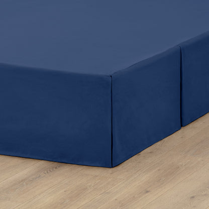 The corner of a box spring with a pleated bed skirt on it
