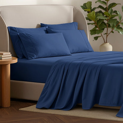 Bed sheets and pillows on a bed with a plant and side table in the background.