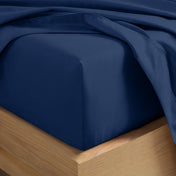 A close-up of a fitted sheet covering the corner of a bed frame, with matching top sheet draped over it.