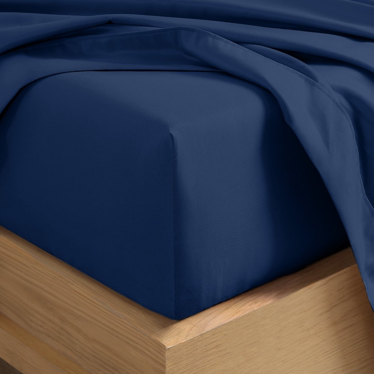 A close-up of a fitted sheet covering the corner of a bed frame, with matching top sheet draped over it.