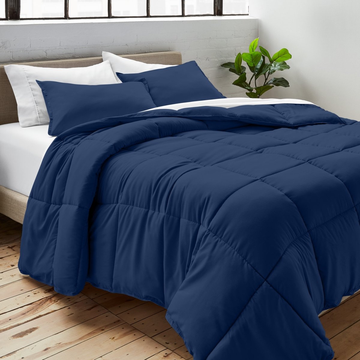 Comforter on a bed with white pillows and a plant in the corner.
