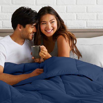 Man and woman sitting together in bed holding a mug, smiling.