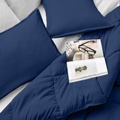 Comforter and pillows on a bed with a magazine and glasses.