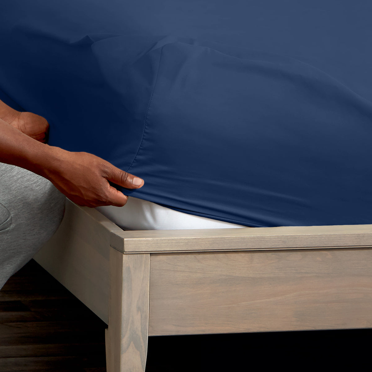 A man is putting a fitted sheet on a bed