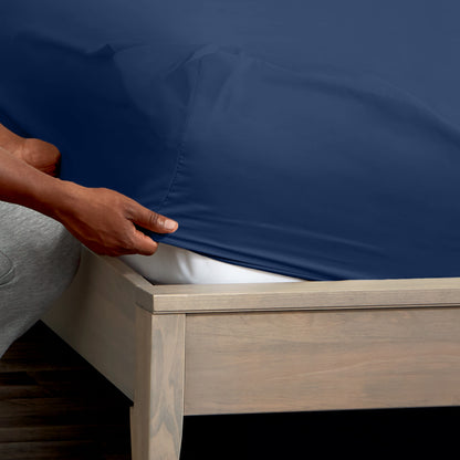 A man is putting a fitted sheet on a bed