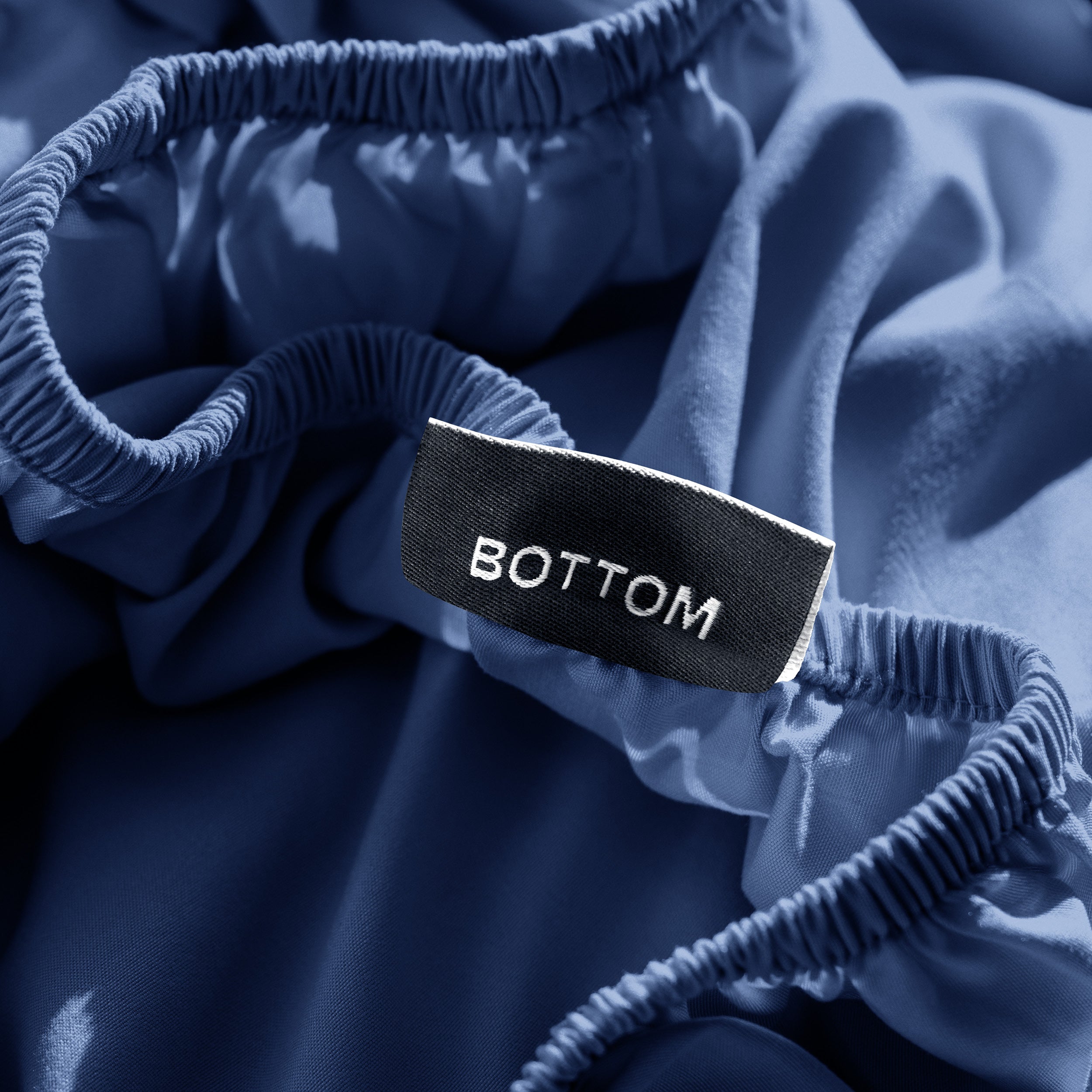 A close-up of a fitted sheet with a label printed with the word 'BOTTOM' in white.