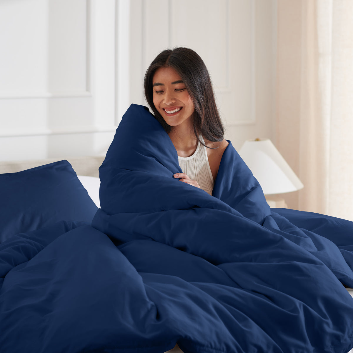 Woman smiling under duvet cover set in a bedroom setting