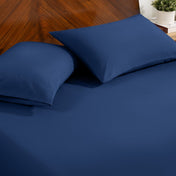 Fitted sheet and pillowcase set on a bed with a dark wood headboard and a small potted plant in the background.
