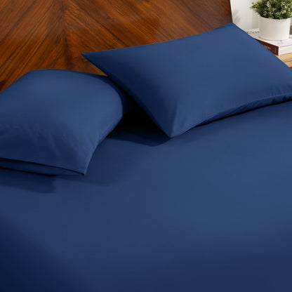 Fitted sheet and pillowcase set on a bed with a dark wood headboard and a small potted plant in the background.