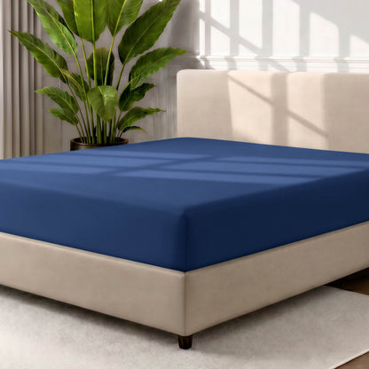 Bed with a fitted sheet in a room with a large plant and rug