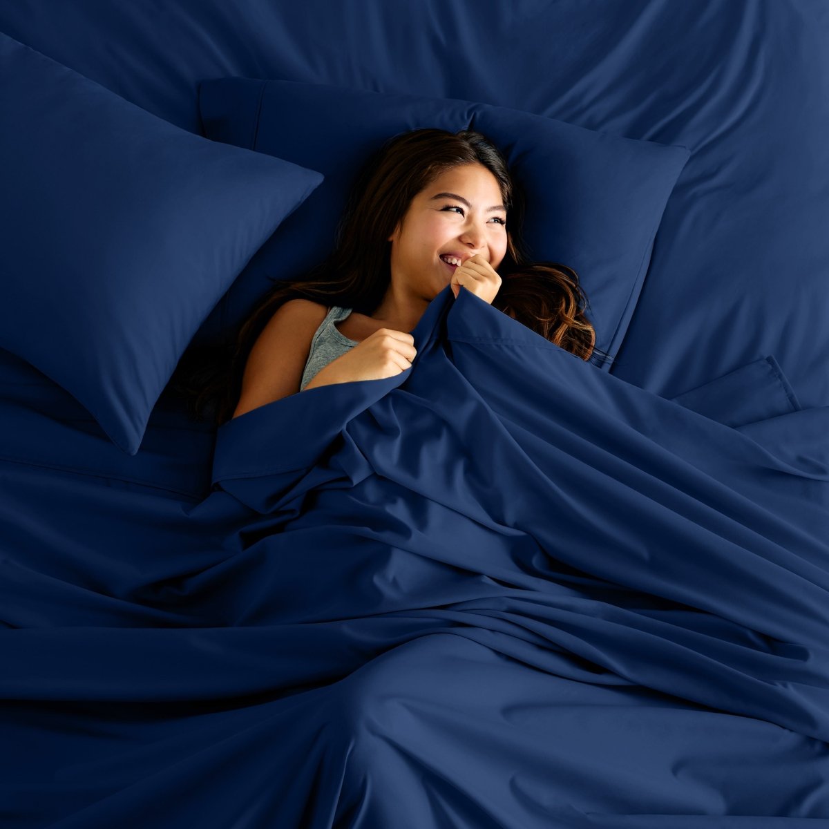 Woman lying in bed under a sheet smiling.