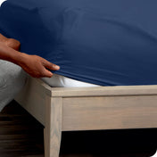 A man is putting a fitted sheet on a mattress
