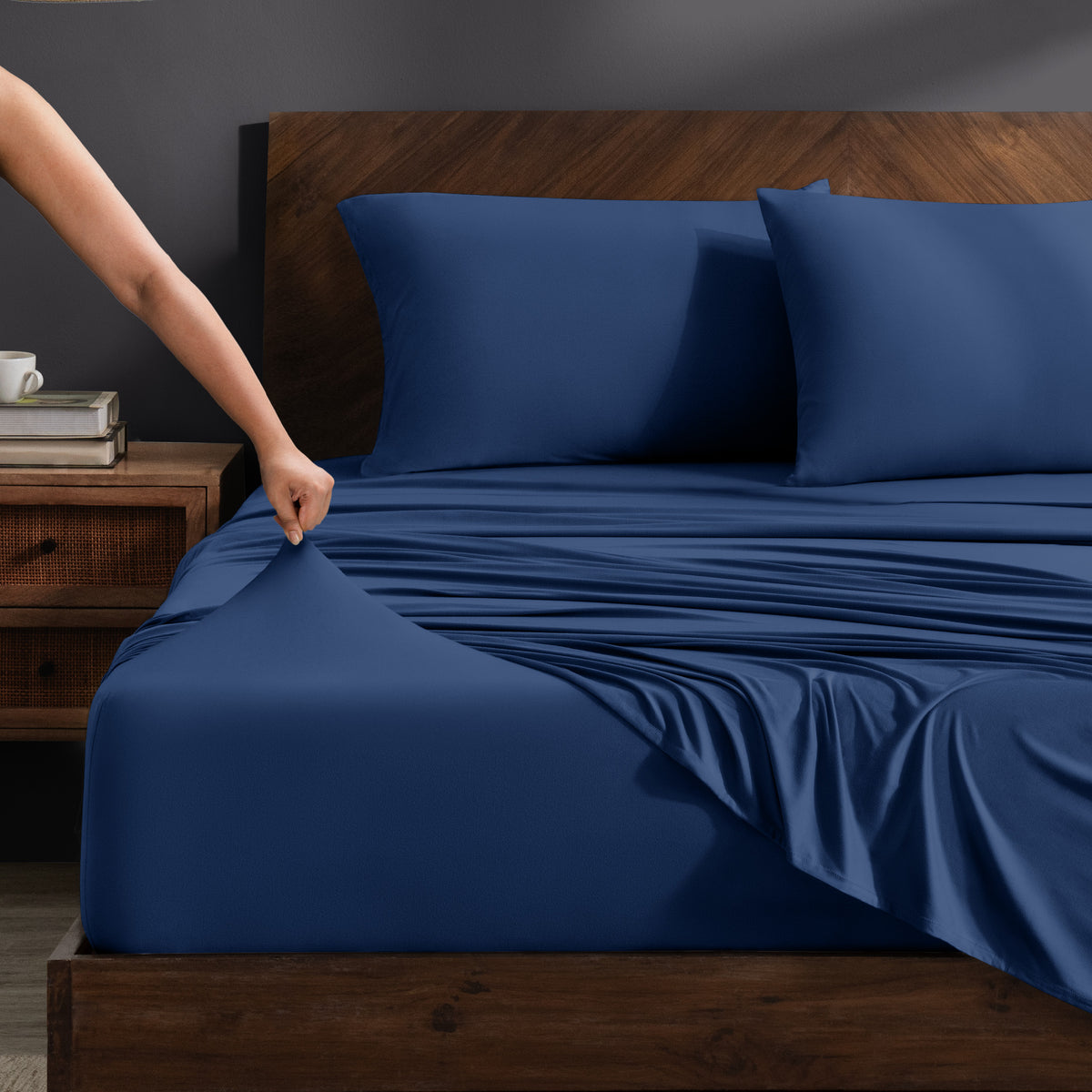 Person adjusting stretch sheets on a bed with a wooden headboard.