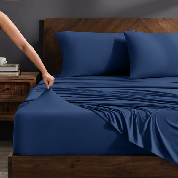 Person adjusting stretch sheets on a bed with a wooden headboard.
