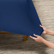Person putting a fitted sheet on a bed on carpeted floor.
