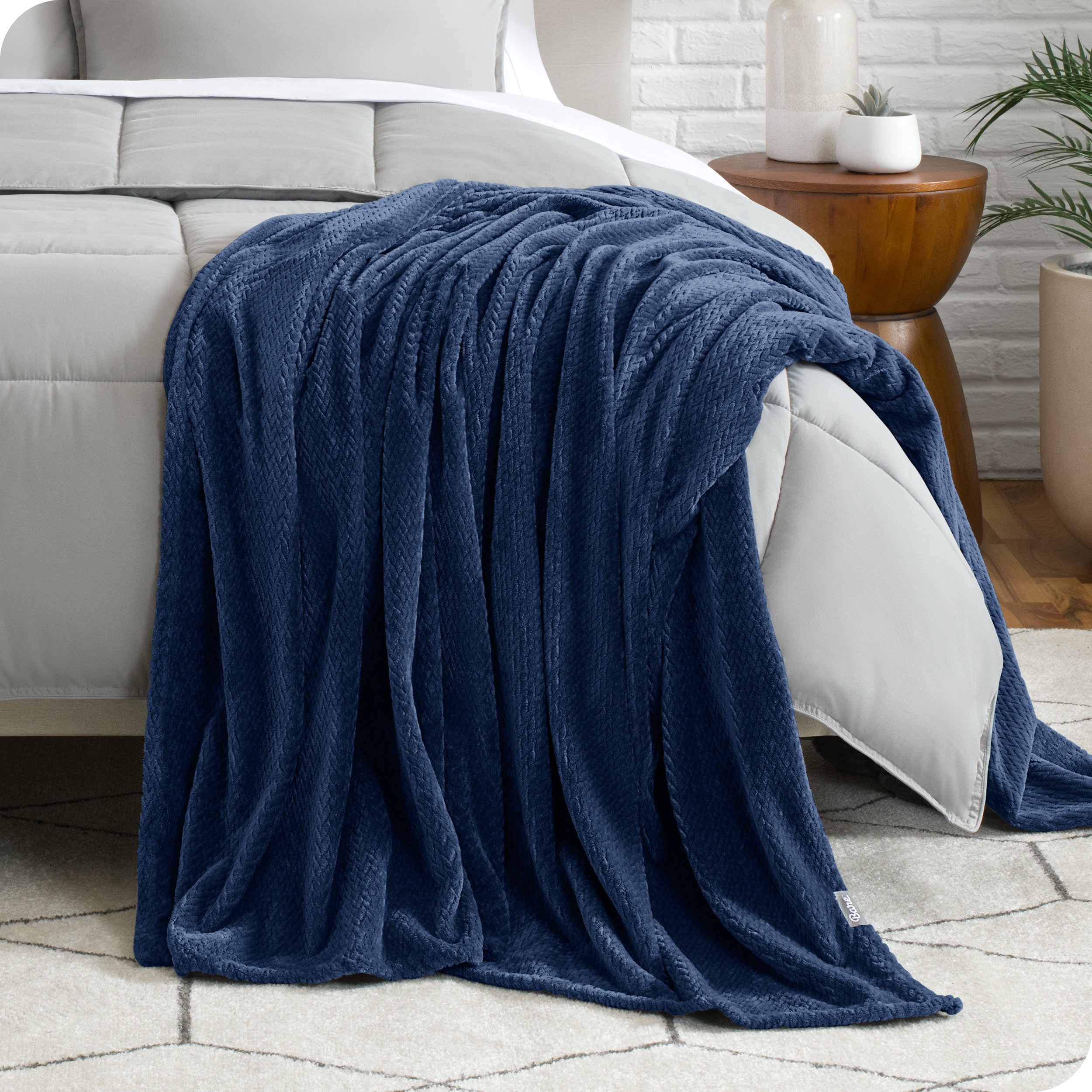 A microplush blanket is draped over the side and bottom of a neatly made bed.