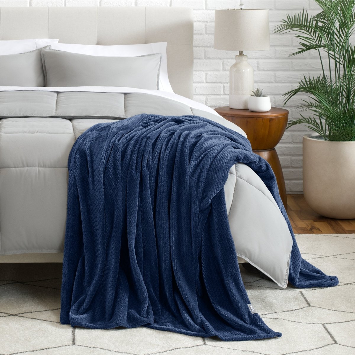 Blanket draped over a bed in a bedroom setting with a lamp and plant.