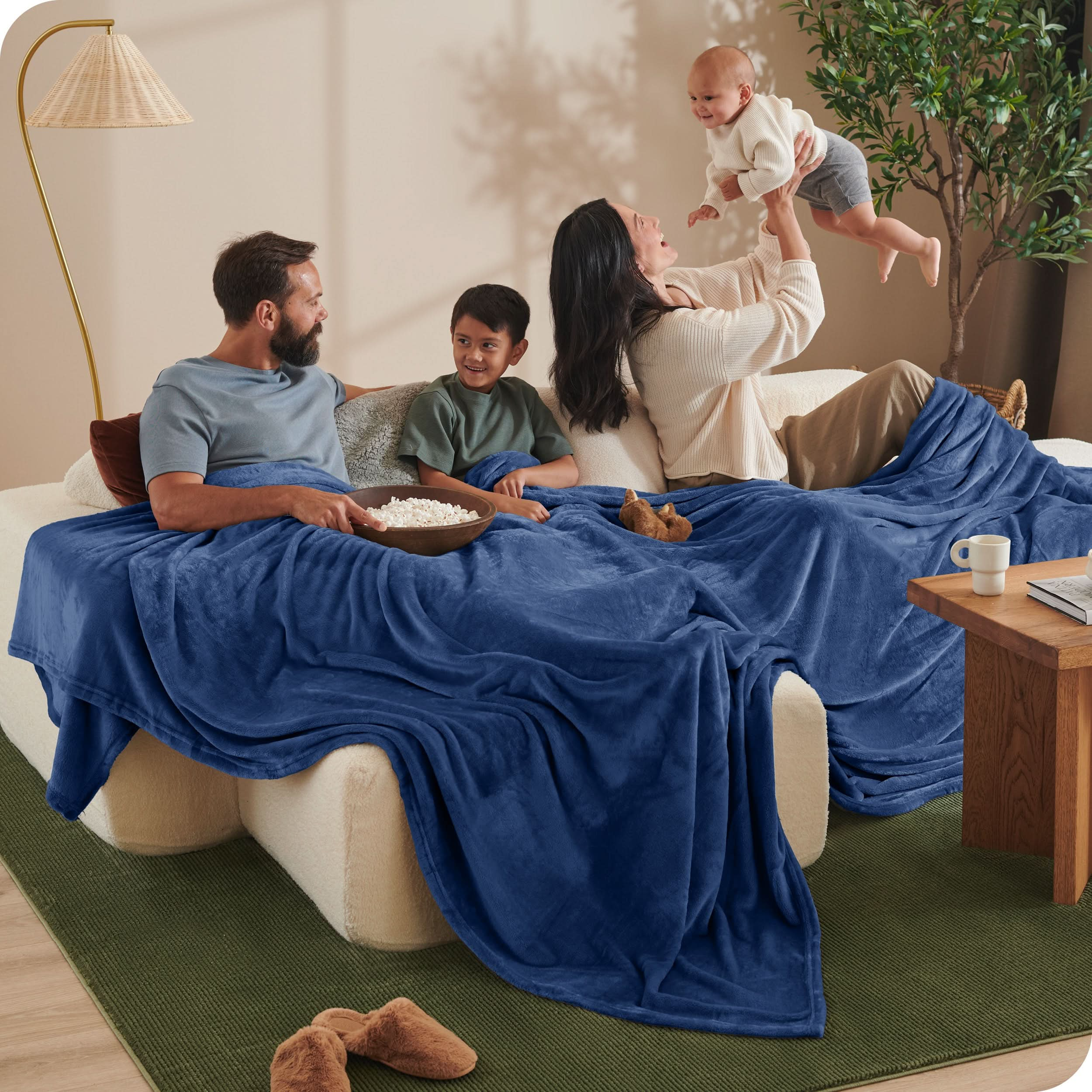 A family sitting with a giant microplush blanket covering them