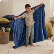 A child has his arms stretched out while holding a microplush blanket behind him