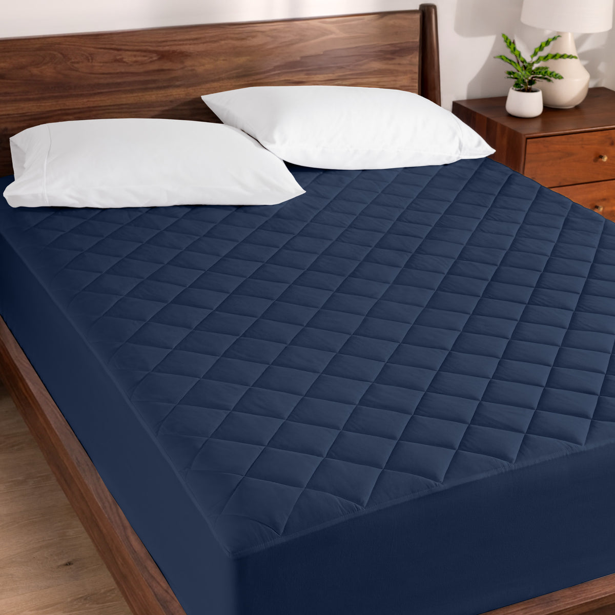 Quilted mattress pad on a bed with wooden headboard and nightstand.