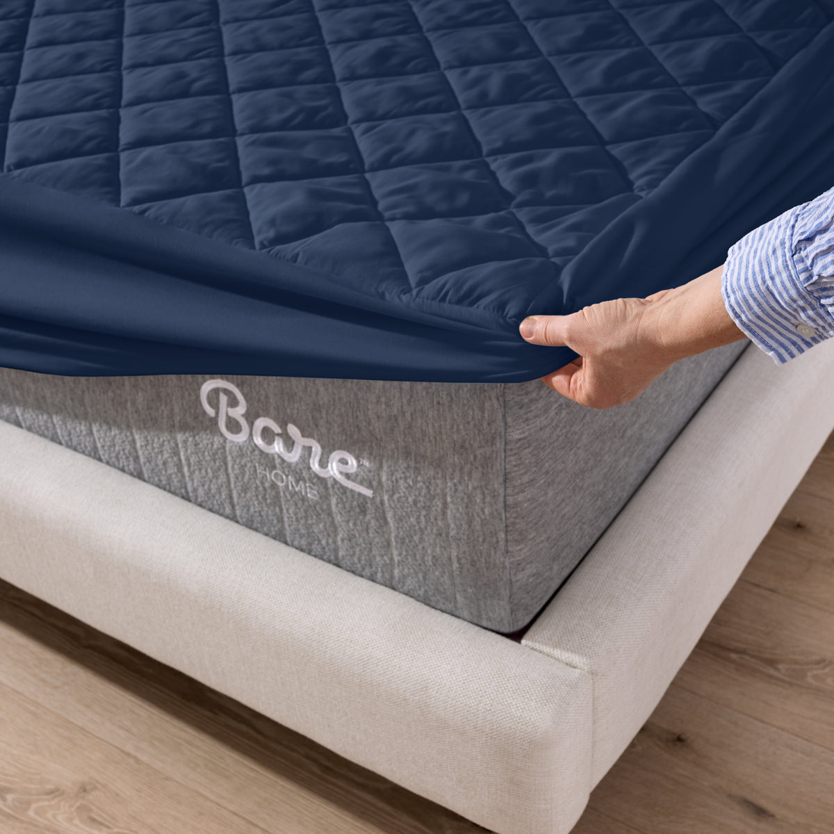 Person putting a mattress cover over a Bare Home branded mattress on a wooden floor.