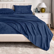 Microplush sheet set on a bed in a bedroom setting with a nightstand and lamp.