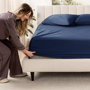 Woman adjusting a fitted sheet on a bed in a bedroom setting