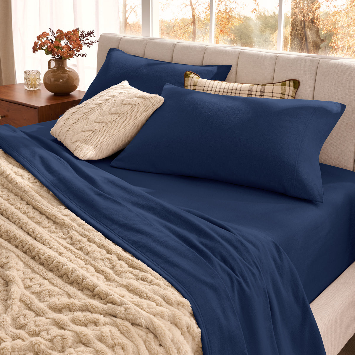 Neatly made bed with organic flannel sheets  and a beige blanket in a bright bedroom.
