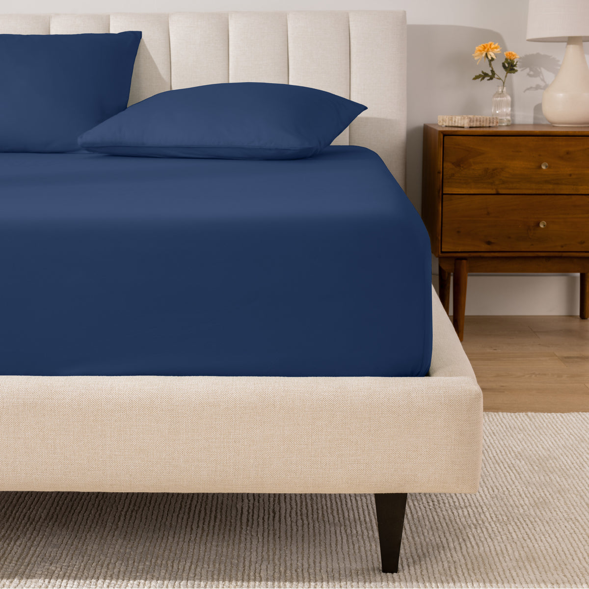 A percale fitted sheet and pillowcases on a bed in a bedroom with a wooden nightstand.