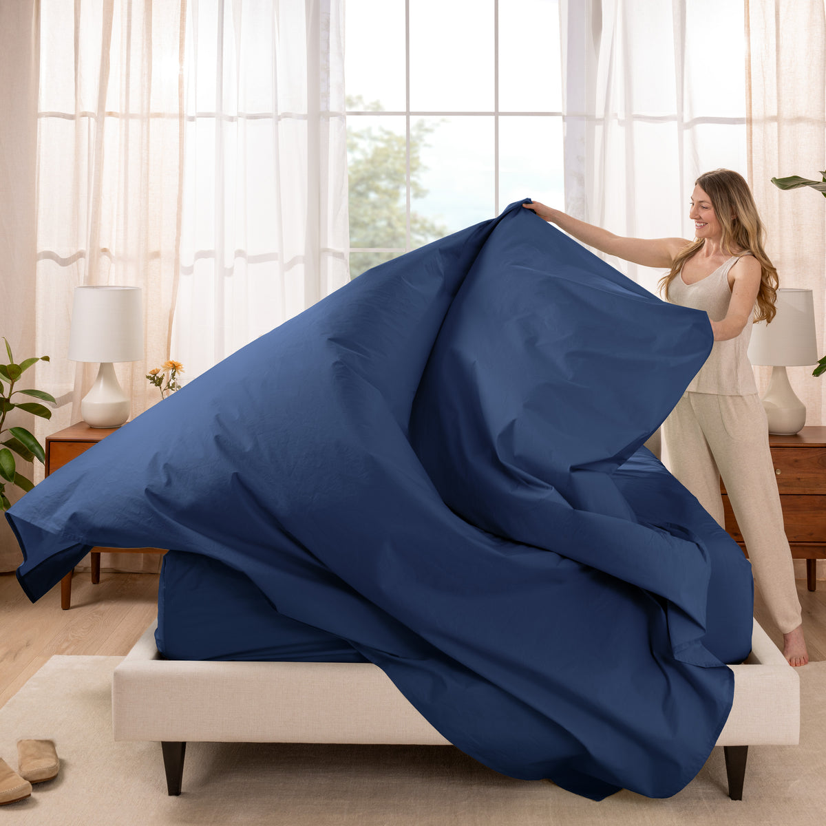 Woman putting a sheet set on a bed in a bright bedroom.