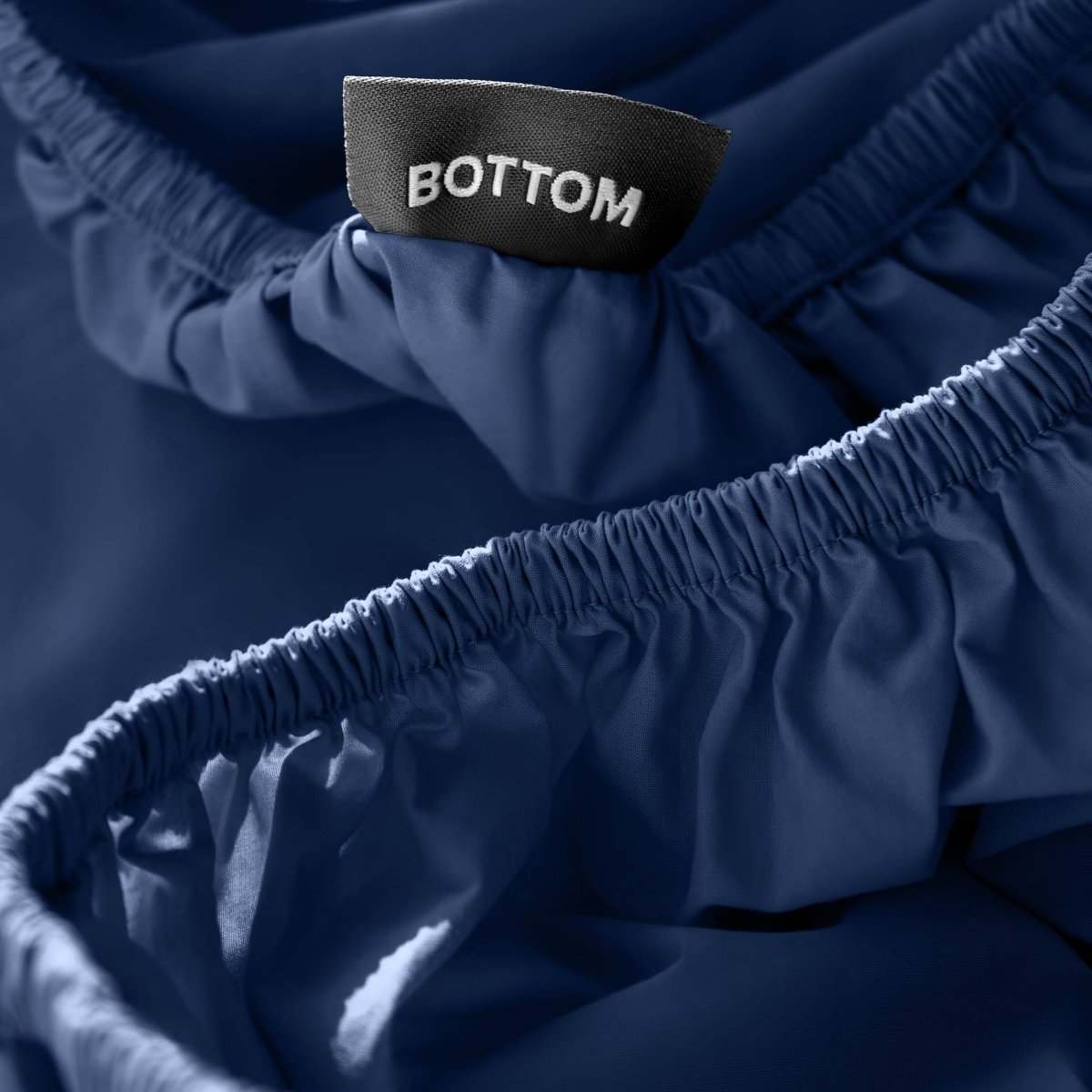 Close-up of a fitted sheet with a black fabric brand label reading BOTTOM.