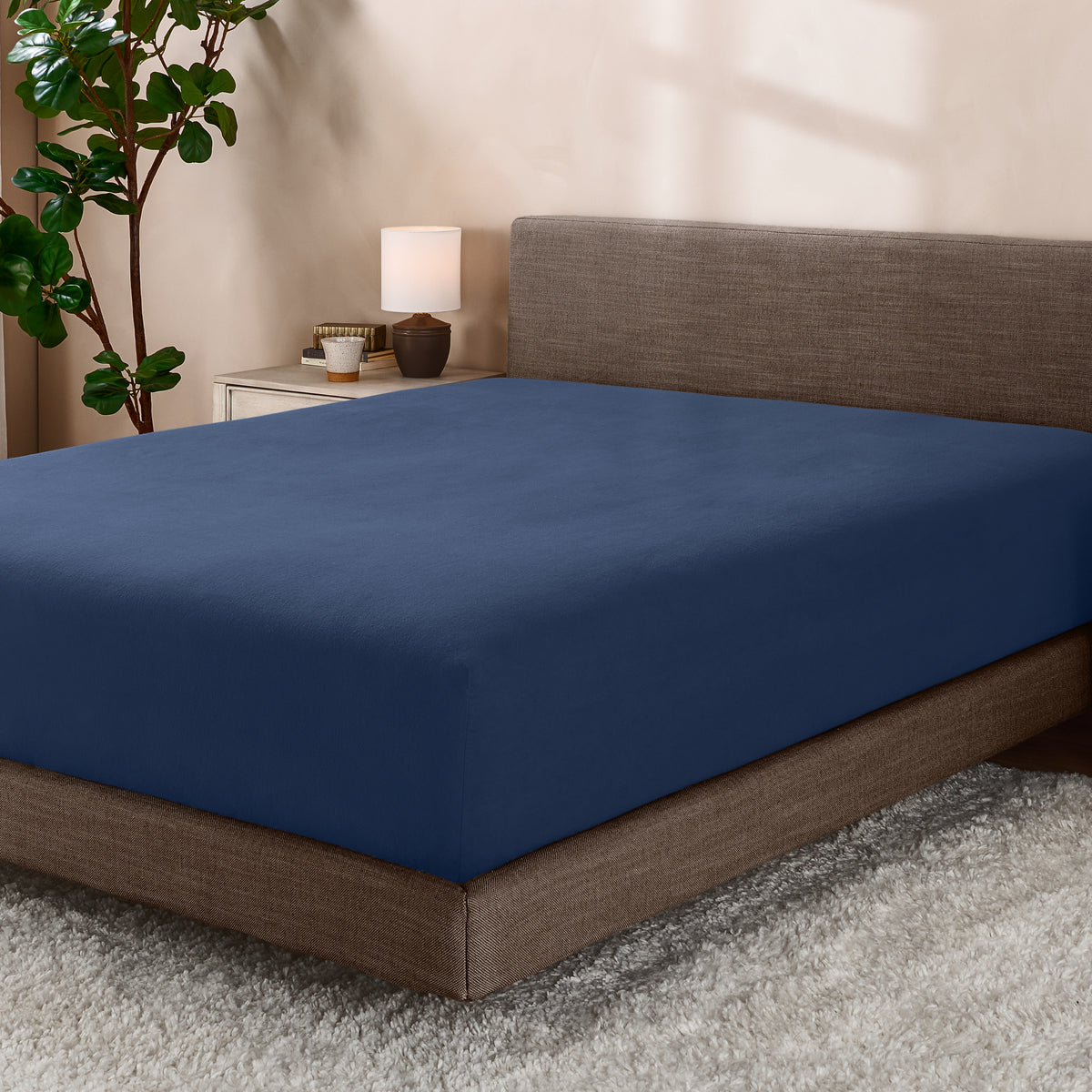 Bed with fitted sheet in a room with a lamp and plant.