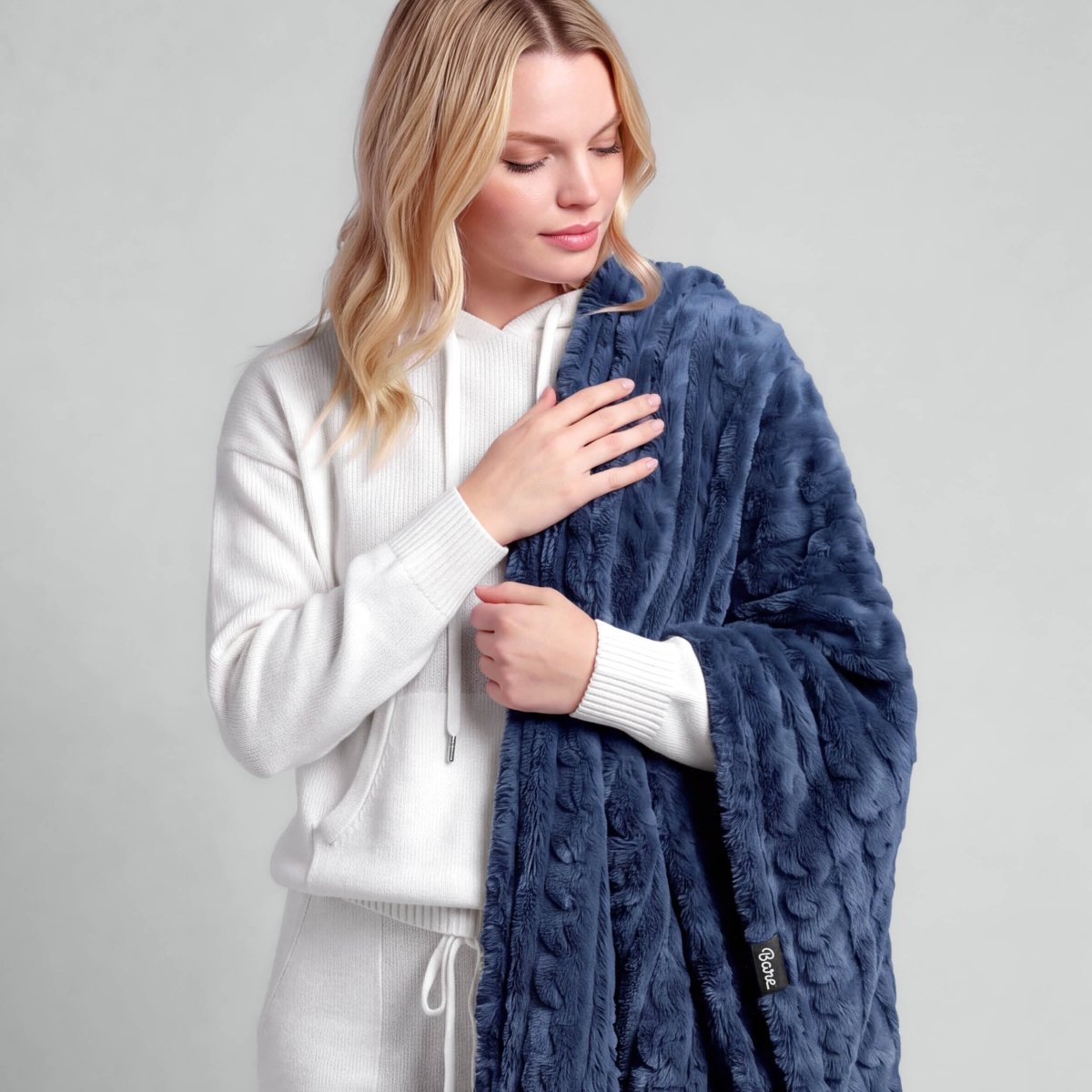 A woman is standing with a textured faux shearling blanket over her shoulder
