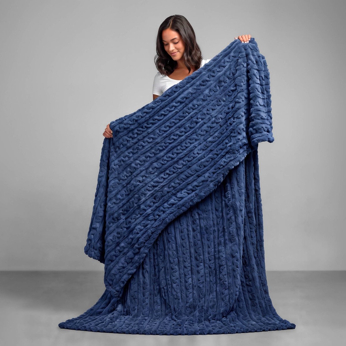 A woman is standing and holding a textured cable knit blanket