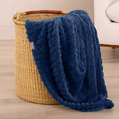 Blue textured blanket draped over a woven basket on a wooden floor.